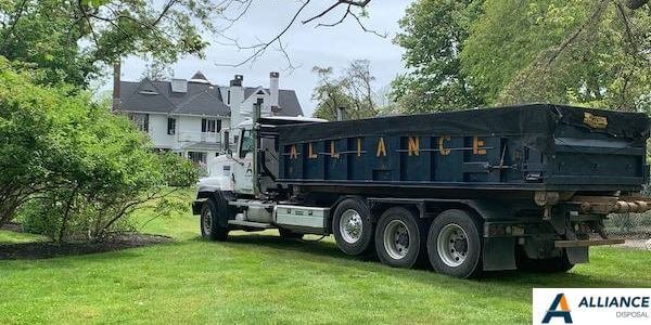 Alliance Disposal truck in front of a customer's house surrounded by trees