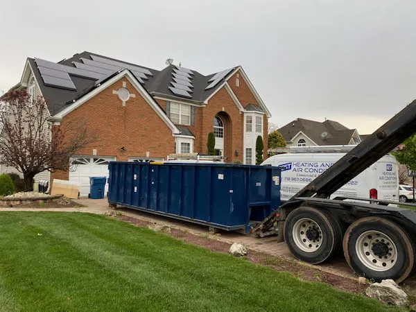 Roll off truck pickup up 30 yard dumpster in driveway in front of house with solar panels