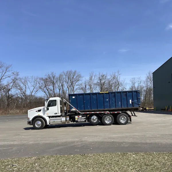 Image of a roll off bin truck in front of trees in a lot
